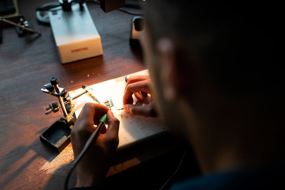A focused engineer soldering a circuit board under bright light in a workshop setting.